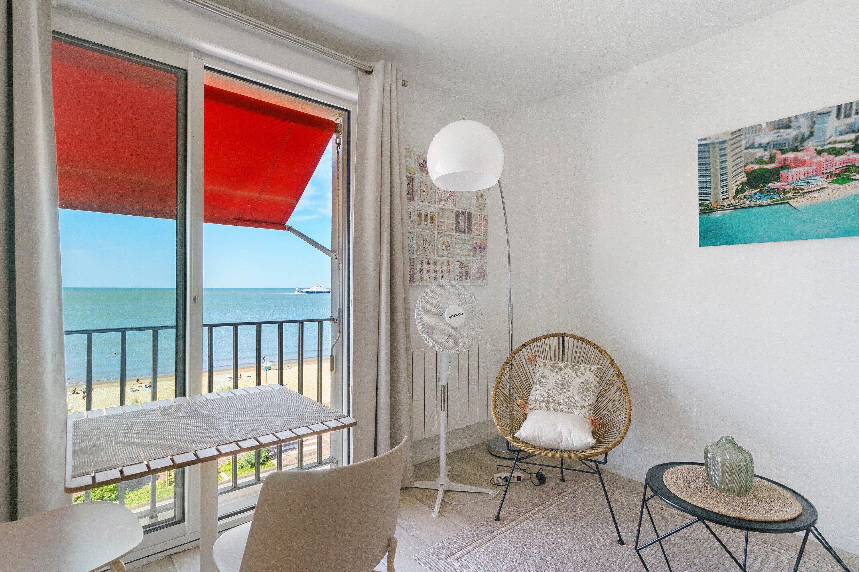 Une chambre avec un balcon donnant sur la mer, une chaise en osier, une petite table et une lampe fixée au mur.