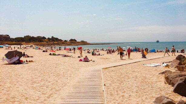 A sandy beach with a wooden boardwalk, umbrellas, and people.