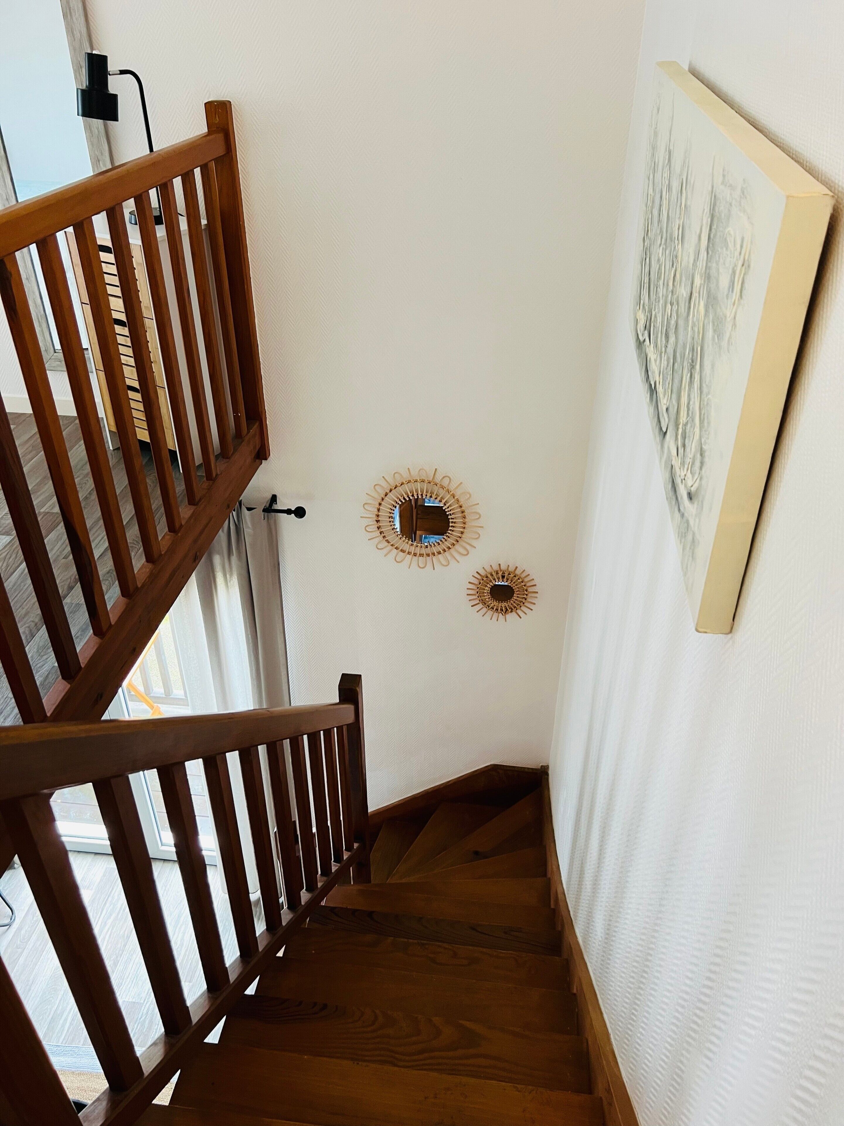 Un escalier en bois avec une rampe, un mur blanc à texture et une œuvre d’art encadrée.