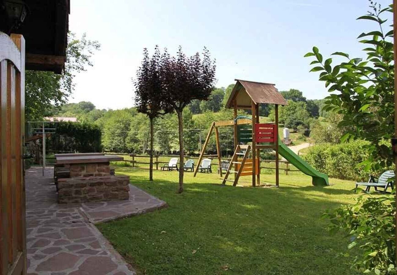 Un parque infantil con tobogán y columpios, un banco de piedra y una mesa de picnic.