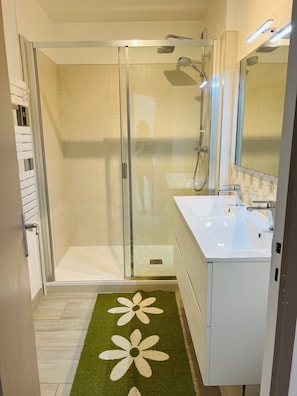 A modern bathroom with a glass-enclosed shower, a white sink, and a mirror.
