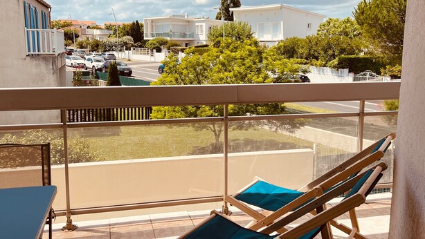 A balcony with a view of a street, a pool, and a building.