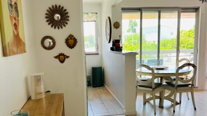 A room with a wooden floor, a dining table with chairs, a wall with decorative mirrors, and a window with a view of greenery.