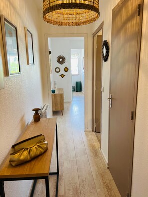 A hallway with a wooden table, a wicker lamp, and a door leading to another room. - Apartment 'Le Cocon' with Balcony (Vaux-sur-Mer)