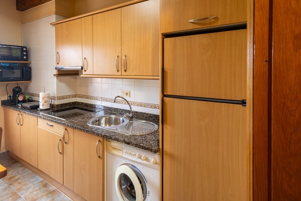 Eine Küche mit Holzausstattung, einer Spüle aus Edelstahl, einer Mikrowelle, einer Waschmaschine und einem Kühlschrank.