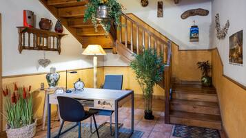 Een houten trap met een hangplant, een eettafel met stoelen en een wandplank met decoratieve objecten.