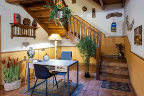 Un escalier en bois orné d’une plante suspendue, une table à manger avec des chaises, et une étagère murale décorée de divers objets.