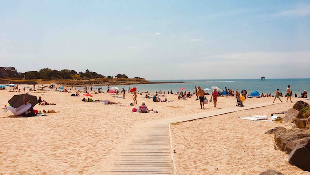 Ein Sandstrand mit einer Holzpromenade, Sonnenschirmen und Menschen.