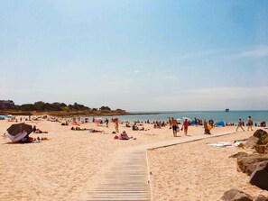 A sandy beach with a wooden boardwalk, umbrellas, and people.