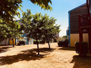 Une cour plantée d’arbres, un bâtiment aux murs bleus et jaunes, et une structure rouge.