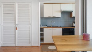 Cocina compacta con armarios blancos, campana extractora de acero inoxidable, un lavabo y una mesa de madera.