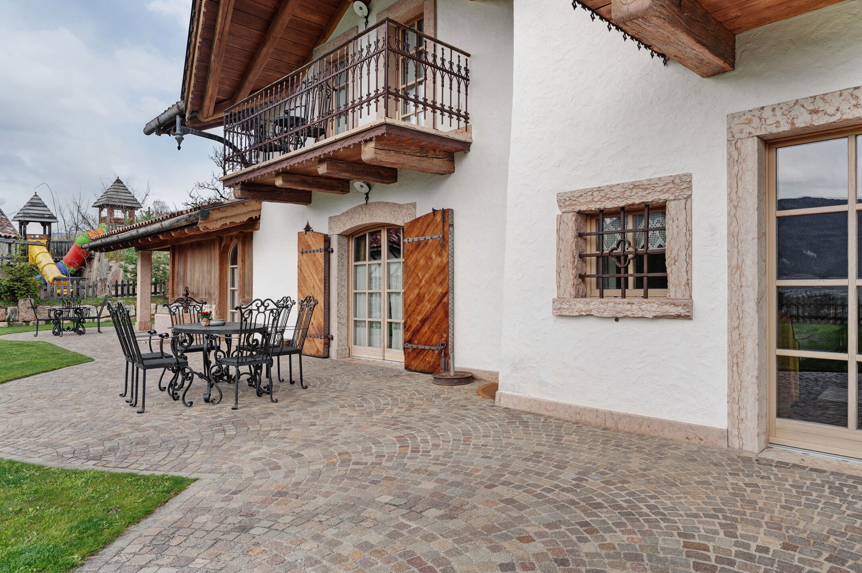 Un tipico chalet con un balcone, un patio con tavolo e sedie e vista sulle montagne.