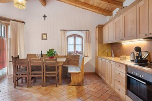 Une cuisine avec des meubles de rangement en bois, une table à manger avec des chaises, un banc, une fenêtre avec des rideaux et une cuisinière.