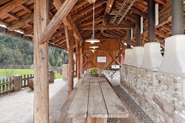 Un pavillon rustique en bois, doté d’un mur en pierre, d’une longue table en bois et de lampes suspendues.