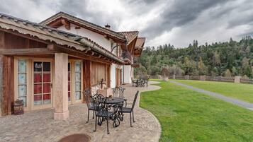 A traditional building with a patio, outdoor seating, and a view of a forested hillside.