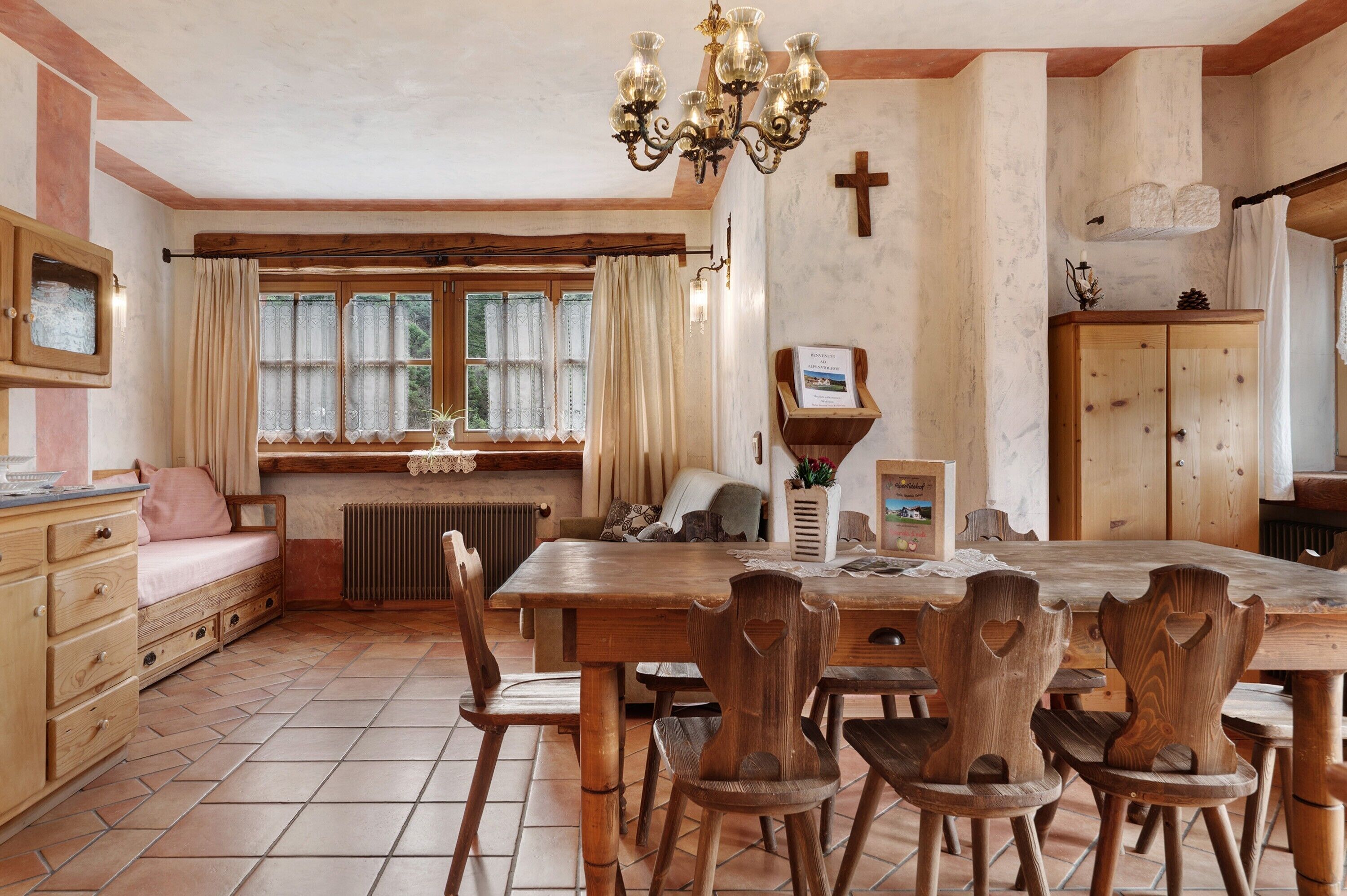 Una sala da pranzo rustica con un tavolo di legno, sedie, un lampadario e una finestra con tende.