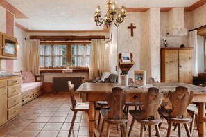 Une salle à manger rustique avec une table en bois, des chaises, un lustre et une fenêtre agrémentée de rideaux.