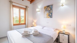 Un dormitorio con cama, dos lámparas de noche, un cuadro y una ventana con cortinas.