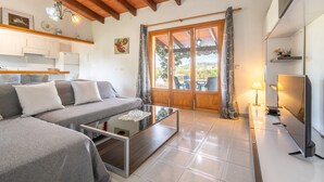 Una sala de estar moderna con sofá, mesa de centro, televisor y una zona de cocina con armarios y refrigerador.