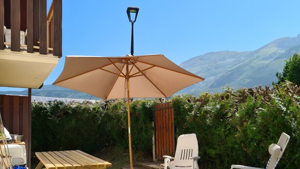 Eine Holzterrasse mit Tisch und Stühlen, einem großen Sonnenschirm und Blick auf Berge.