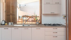 A kitchen with a sink, stove, cabinets, and a view of an outdoor dining area through an open door.