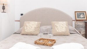 A bed with a headboard, two pillows with a coral design, a tray with two glasses, and a framed picture on the nightstand.