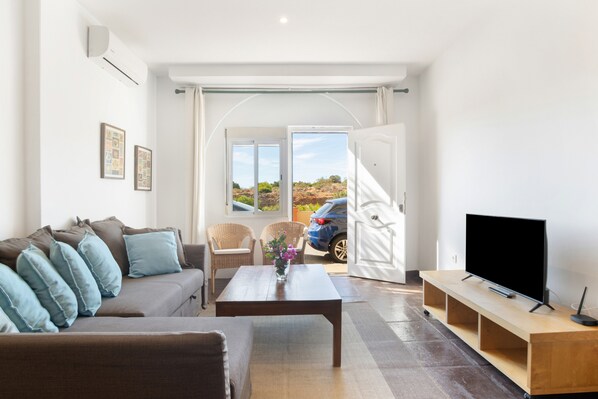 A living room with a sofa, coffee table, TV stand, and a view through an open door.