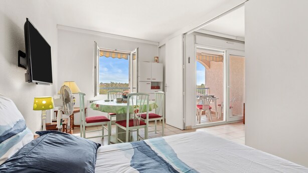 Une chambre comprenant un lit, un bureau avec une chaise, une table avec des chaises et une porte-fenêtre coulissante donnant sur un espace extérieur.