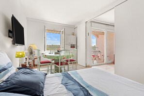 A bedroom with a bed, a desk with a chair, a table with chairs, and a sliding glass door leading to an outdoor area.