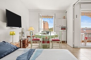 A bedroom with a bed, a TV, a fan, a table with chairs, and a balcony with a view.