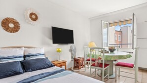 Une chambre à coucher comprenant un lit, une télévision, une petite table avec des chaises et une fenêtre donnant sur des immeubles.