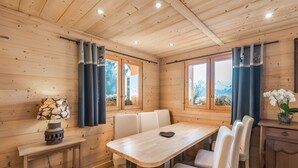 A wooden-paneled room with a dining table, chairs, a small table with a lamp, and a cabinet. - Chalet 'Velajule', private shuttle at the slopes, private jacuzzi & shared pool (Manigod)