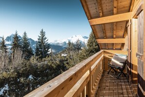 Un balcon en bois avec une chaise, donnant sur un paysage montagneux enneigé.