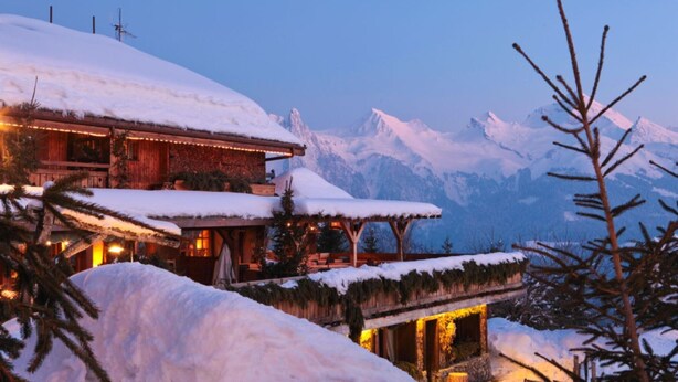 A snow-covered lodge with a wooden exterior, a balcony with a snow-covered roof, and a mountain backdrop. - Chalet 'Velajule', private shuttle at the slopes, private jacuzzi & shared pool (Manigod)