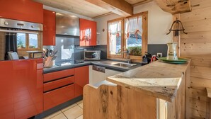 A modern kitchen with red cabinets, stainless steel appliances, and a wooden ceiling. - Chalet 'Velajule', private shuttle at the slopes, private jacuzzi & shared pool (Manigod)