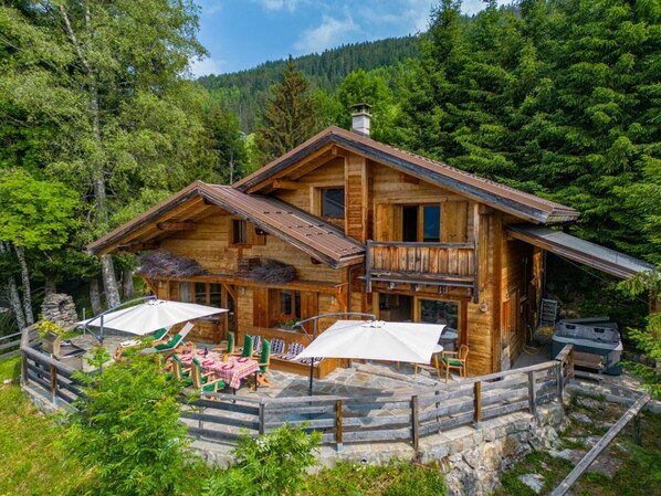 Un chalet en bois doté d’un balcon, d’un espace extérieur aménagé et de fondations en pierre.