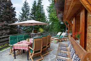 Une terrasse extérieure avec une table dressée pour les repas, des chaises en bois, un grand parasol et une plateforme en bois.