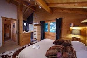 A wooden cabin bedroom with a bed, a bedside lamp, a window with curtains, and a wooden wardrobe.