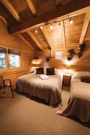 Une chambre confortable dans un chalet en rondins, avec deux lits, un plafond en bois et une fenêtre donnant sur un paysage agréable.