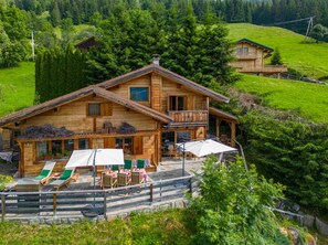 A wooden chalet with a balcony, outdoor seating, and a stone staircase leading to the entrance.