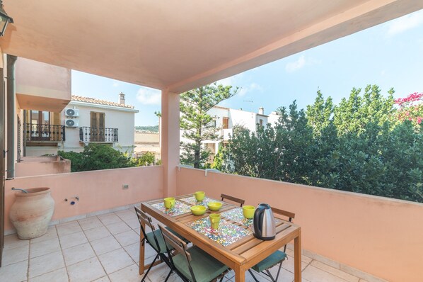 Un balcon avec une table dressée pour quatre personnes, des chaises, un grand vase et une vue sur les bâtiments voisins et la verdure.