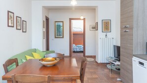 A dining area with a wooden table, chairs, a bowl, and a green sofa. There are framed pictures on the walls and a doorway leading to another room. - Holiday Home 'Le Giare' with Sea View, Wi-Fi, Air Conditioning and Balcony (La Maddalena)