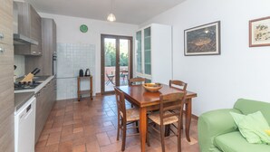 A modern kitchen with a dining table, chairs, and a green sofa. - Holiday Home 'Le Giare' with Sea View, Wi-Fi, Air Conditioning and Balcony (La Maddalena)