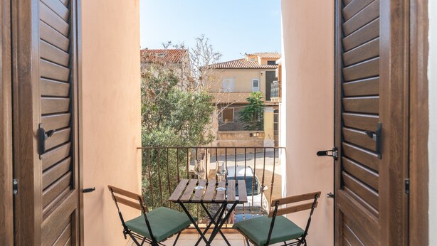 A balcony with wooden shutters, a table with two chairs, and a view of buildings and trees. - Holiday Home 'Le Giare' with Sea View, Wi-Fi, Air Conditioning and Balcony (La Maddalena)