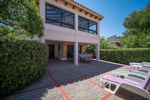A two-story building with a patio area featuring outdoor seating and sun loungers.