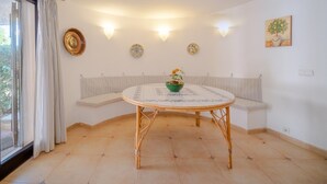 Una habitación con una mesa redonda, dos bancos acolchados, una ventana con cortinas, luces fijadas a la pared y platos decorativos.