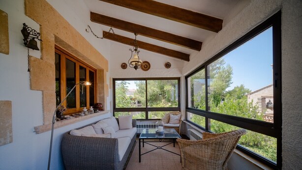 Una habitación iluminada por el sol con un sofá, una silla de mimbre y una mesa, con ventanas amplias y un ventilador de techo.