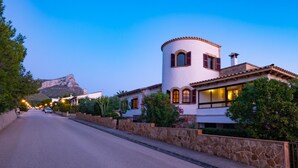 Una calle con un edificio blanco que presenta una torre redonda, muros de piedra y una montaña al fondo.