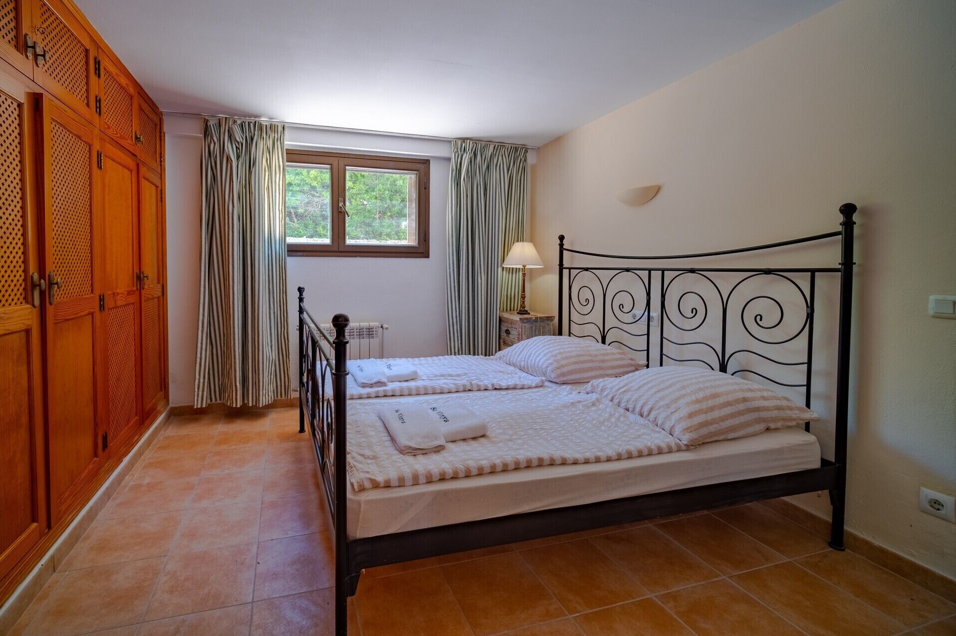 A bedroom with a bed, curtains, a window, and wooden furniture.
