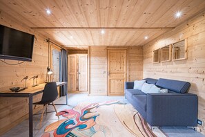 A wooden interior with a sofa, a desk, a chair, and a flat-screen TV. - Chalet 'Fnire' with Mountain View, Private Jacuzzi and Shared Pool (Manigod)